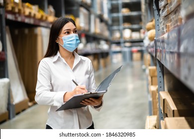 woman worker with medical mask holding clipboard and checking inventory in the warehouse during coronavirus (covid-19) pandemic