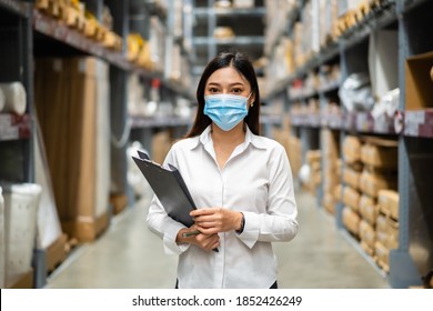 Woman Worker With Medical Mask Holding Clipboard And Checking Inventory In The Warehouse During Coronavirus (covid-19) Pandemic