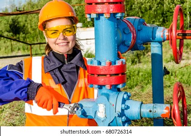 Woman worker in the oilfield repairing wellhead, wearing orange helmet and work clothes. Industrial site background. Oil and gas concept.