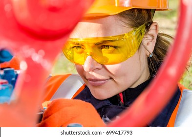 Woman Worker In The Oilfield Repairing Wellhead Wearing Orange Helmet And Work Clothes. Industrial Site Background. Oil And Gas Concept.