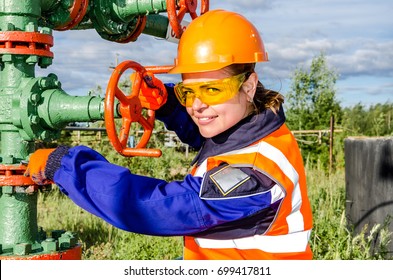 Woman Worker In The Oilfield Repairing Wellhead Wearing Orange Helmet And Work Clothes. Industrial Site Background. Oil And Gas Concept.