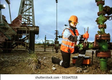 Woman Worker On The Oil Field Repairing Of Oil And Gas Well, With The Wrench Wearing  Helmet And Work Clothes. Working Process On Oil Wellhead.