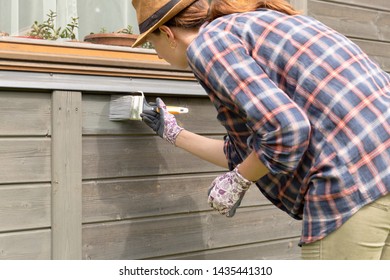 Woman Worker Painting Wooden House Exterior Wall With Paintbrush And Wood Protective Color