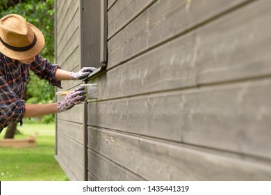 Woman Worker Painting Wooden House Exterior Wall With Paintbrush And Wood Protective Color