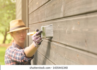 Woman Worker Painting Wooden House Exterior Wall With Paintbrush And Wood Protective Color