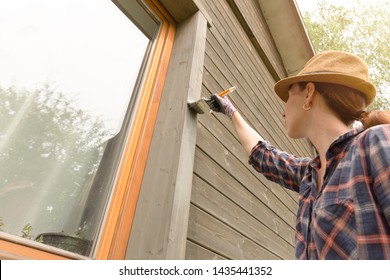 Woman Worker Painting Wooden House Exterior Wall With Paintbrush And Wood Protective Color