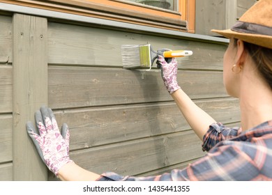 Woman Worker Painting Wooden House Exterior Wall With Paintbrush And Wood Protective Color