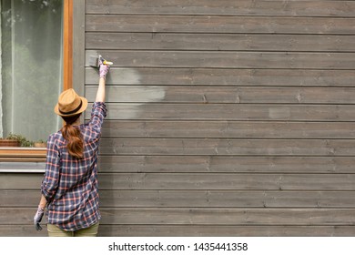 Woman Worker Painting Wooden House Exterior Wall With Paintbrush And Wood Protective Color