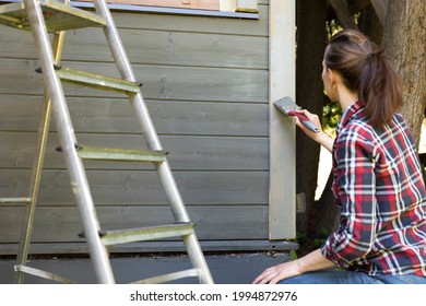 Woman Worker Painting Wooden House Exterior Wall With Paintbrush And Wood Protective Color Home Improvement Concept.