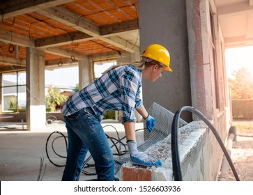 Woman worker settling metal net material on the concrete wall.Beautiful female civil engineer working on construction site.Busy builder woman 