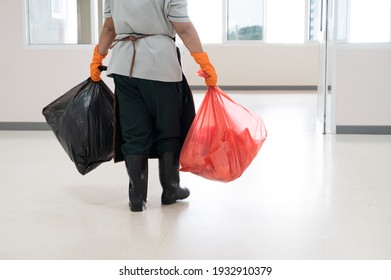 A Woman Worker Wearing Orange Gloves Holding Red And Black Garbage Bag Into Bin.Maid And Infection Waste Bin At The Indoor Public Building.Infectious Control.