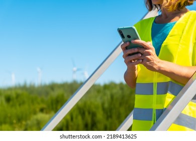 Woman Worker In A Wind Farm, Green Energy, Reviewing The Notes With The Phone