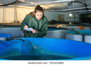 Woman in working clothes controlling fish growth in trout hatchery incubator