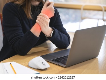 A woman working at a desk using a laptop and a mouse is suffering from wrist pain, and the painful part is marked in red