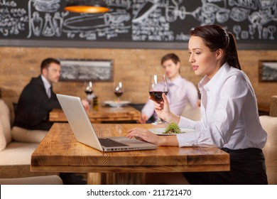 Woman Working And Drinking Wine At Lunch In Cafe. Portrait Of Pretty Businesswoman Sitting At Cafe With Laptop