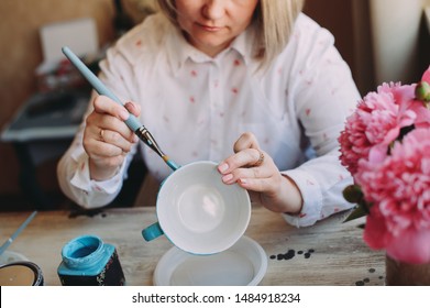 Woman working In her pottery studio. Ceramic workshop. Paint on clay cup in the pottery. Painting in pottery - Powered by Shutterstock