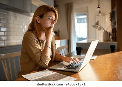 Woman working from home looking concerned with paperwork and laptop - Powered by Shutterstock