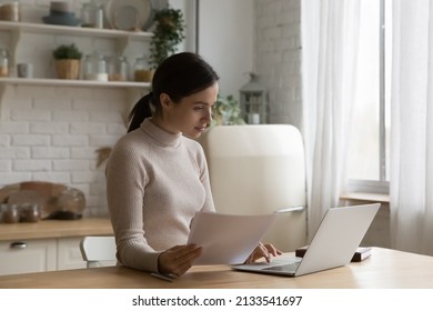 Woman working from home seated at table in domestic kitchen use laptop, prepare official papers documents for client, holds sheet comparing information, busy in paperwork, pay bills via e-bank concept - Shutterstock ID 2133541697