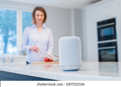 Woman Working In Kitchen With Smart Speaker In Foreground