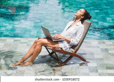 Woman working with laptop by the pool. Freelance work in tropical country
