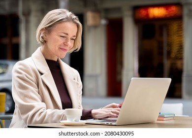 Woman working with laptop in a terrace of a cafeteria. Professional business woman with blond short hair in her late 30s 40s outdoors in a city. - Powered by Shutterstock