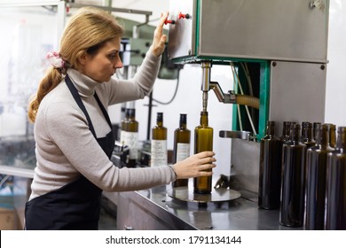 Woman working on bottling conveyor of food producing factory, filling glass bottles with olive oil - Powered by Shutterstock