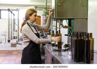 Woman Working On Bottling Conveyor Of Food Producing Factory, Filling Glass Bottles With Olive Oil