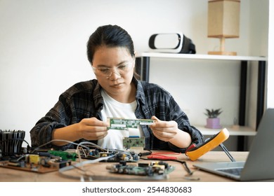 A woman is working on a computer part. She is wearing glasses and is focused on her task - Powered by Shutterstock