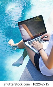 Woman Working On Her Laptop Computer Sitting At Poolside