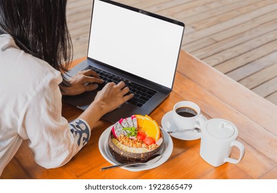 Woman working on laptop with bowl of smoothie breakfast and coffee on table. - Powered by Shutterstock