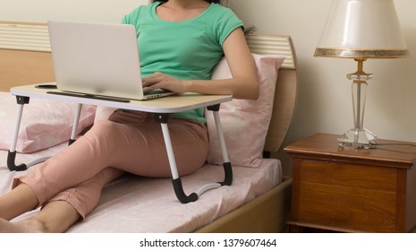 Woman Working On Laptop Computer On Portable Table In Bedroom