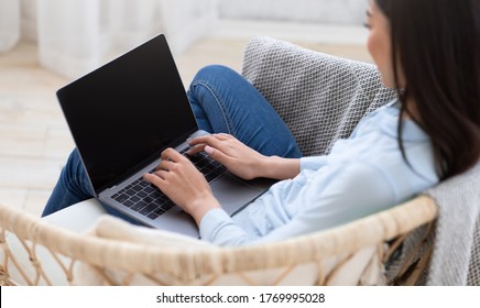 Woman Working On Laptop Computer With Blank Black Screen At Home, Sitting In Chair, Over Shoulder View, Mockup