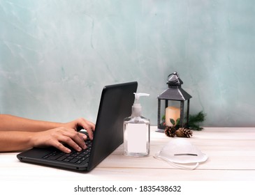 Woman Working On Laptop Computer In Office At Christmas With Face Mask And Hand Sanitizer. 