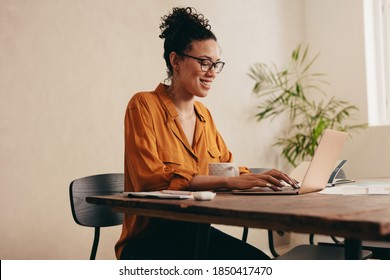 Woman working on laptop computer at home. Woman sitting at table with a coffee cup using a laptop at home office.