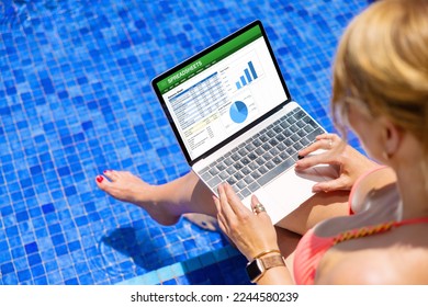 Woman working on laptop computer while sitting by the pool