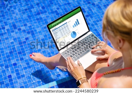 Woman working on laptop computer while sitting by the pool