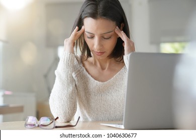 Женщина, работающая на ноутбуке с головной болью