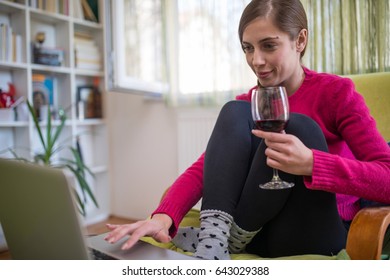 Woman working on laptop at her home and holding a glass of wine - Powered by Shutterstock