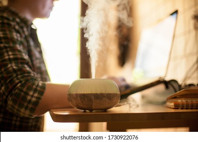Woman working on laptop from home during covid-19 with essential oil diffuser on table.
