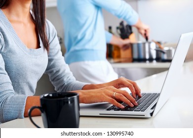 woman working on laptop in kitchen as boyfriend prepares meal. happy healthy relationship multiracial couple - Powered by Shutterstock