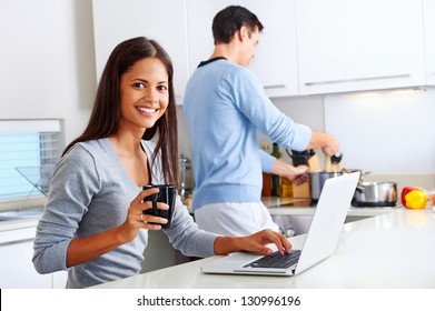 woman working on laptop in kitchen as boyfriend prepares meal. happy healthy relationship multiracial couple - Powered by Shutterstock