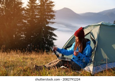 Woman working on laptop near camping tent outdoors surrounded by beautiful nature - Powered by Shutterstock