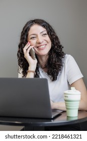 Woman Is Working On A Laptop, Talking On The Phone And Smiling. A Happy Successful Spanish Woman Entrepreneur Or Student Works In A Freelance Coworking. Marketer And Social Media Manager