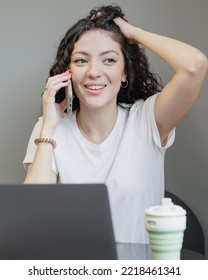 Woman Is Working On A Laptop, Talking On The Phone And Smiling. A Happy Successful Spanish Woman Entrepreneur Or Student Works In A Freelance Coworking. Marketer And Social Media Manager