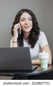 Woman Is Working On A Laptop, Talking On The Phone And Smiling. A Happy Successful Spanish Woman Entrepreneur Or Student Works In A Freelance Coworking. Marketer And Social Media Manager