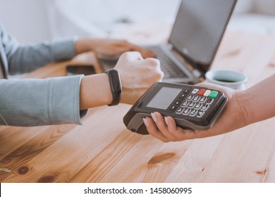Woman working on laptop, using terminal for contactless payment via smartwatch for her order in cafe. New technology of NFC payment - Powered by Shutterstock