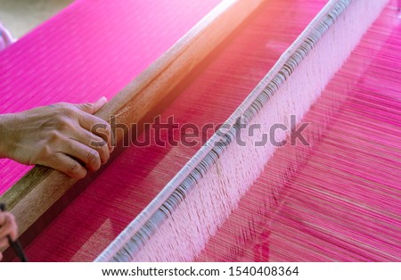 Woman working on weaving machine for weave handmade fabric. Textile weaving. Weaving using traditional hand weaving loom on the long cotton strands. Textile production in Thailand. Asian culture.