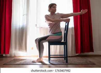 Woman working out doing yoga or pilates exercise using chair. Ardha Matsyendrasana pose variation.