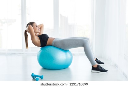 Woman working out with fitness ball in gym, doing exercises for muscle press in white room, copy space
