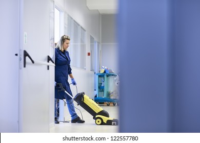 Woman working, professional maid cleaning and washing floor with machinery in industrial building. Full length, copy space